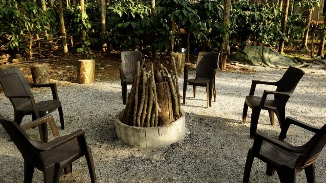 The campfire with chairs set around it on gravel among the trees